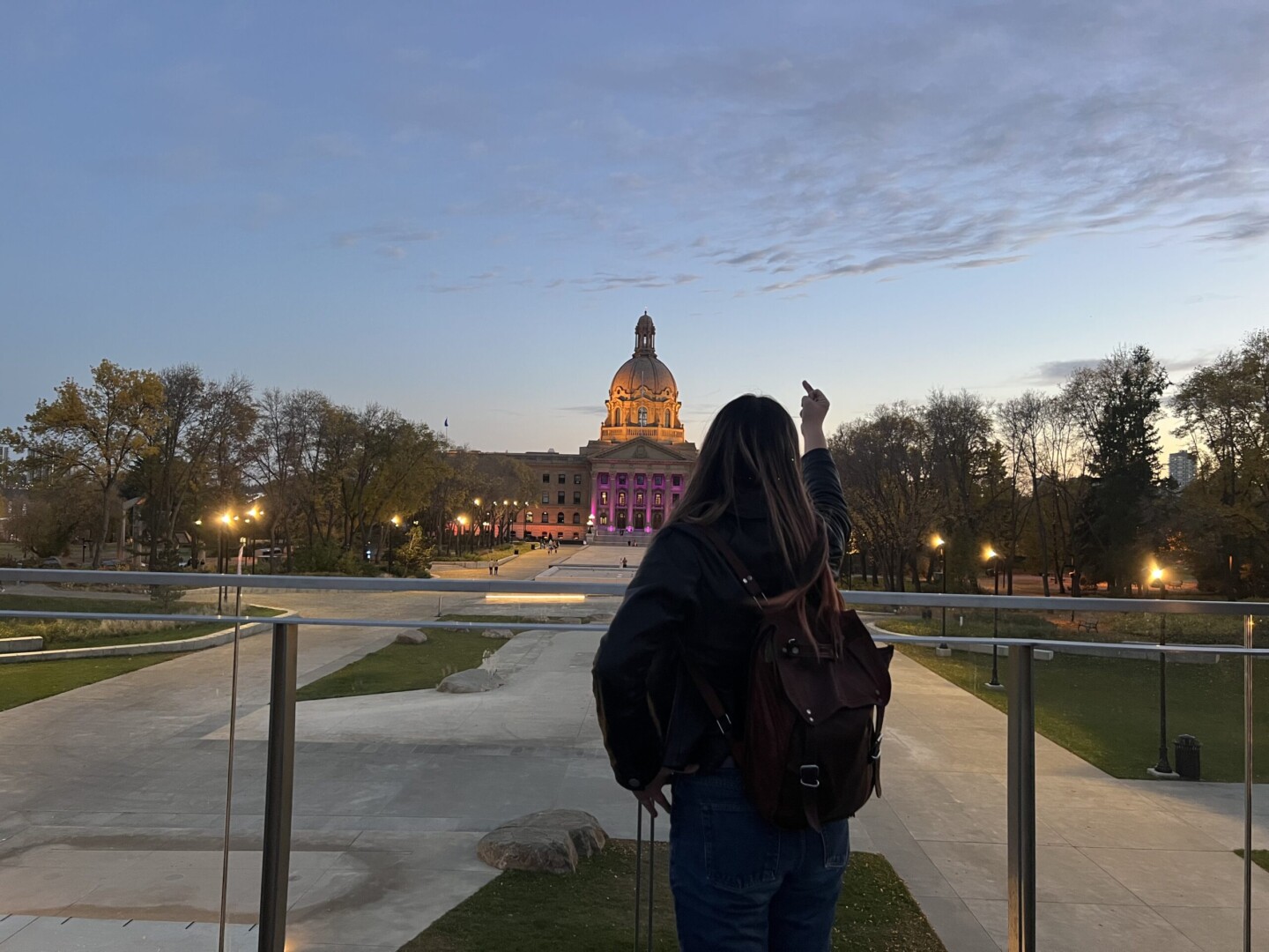 Celeste Trianon pointing a middle finger at the Alberta legislature, at sunset.