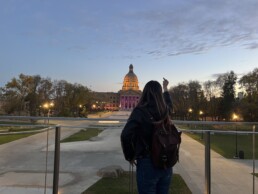 Celeste Trianon pointing a middle finger at the Alberta legislature, at sunset.